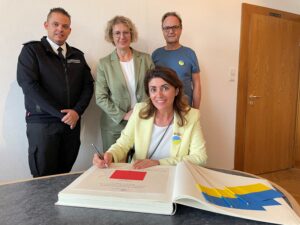 Linda Mai trägt sich ins Goldene Buch der Stadt ein. Hinter ihr stehen Bürgermeisterin Sandra Pietschmann, stellvertretender Amts- und Wehrleiter Sebastian Thews und Otto Grochtdreis. (Foto: Kreisstadt Mettmann)